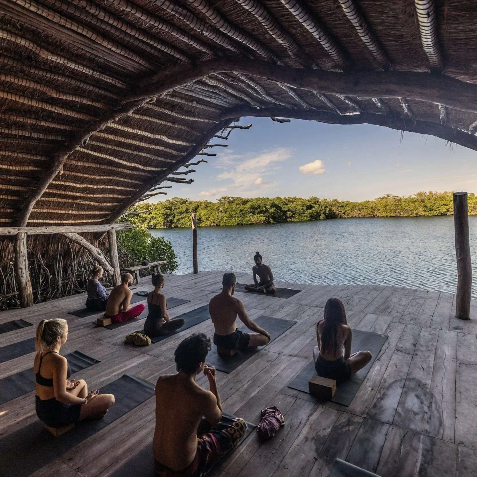 Group yoga and meditation class practicing beside the water in an open-air wellness space