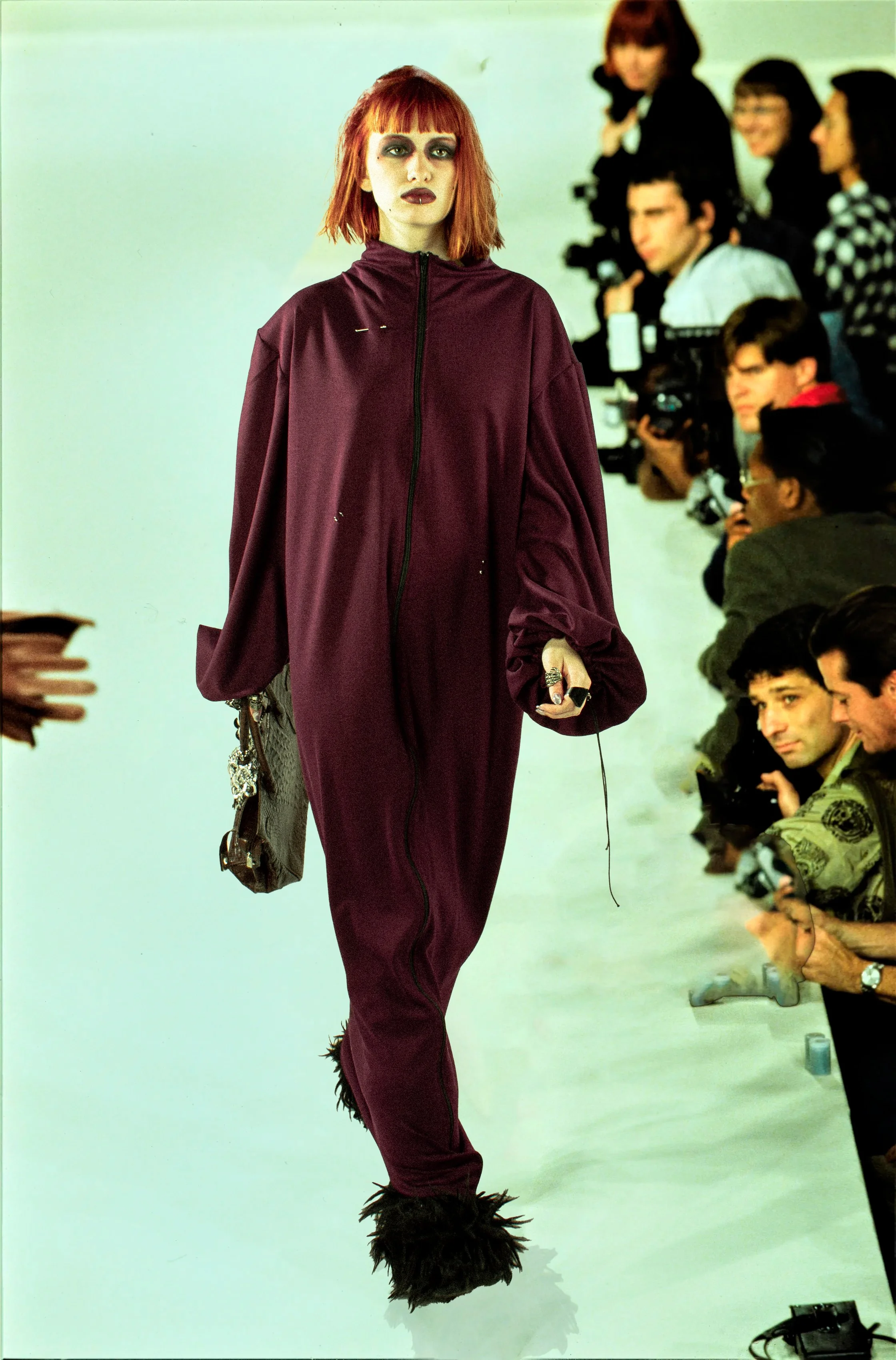 Mujer joven con cabello rojo, vestido de color burdeos, con maquillaje oscuro, en un desfile de moda