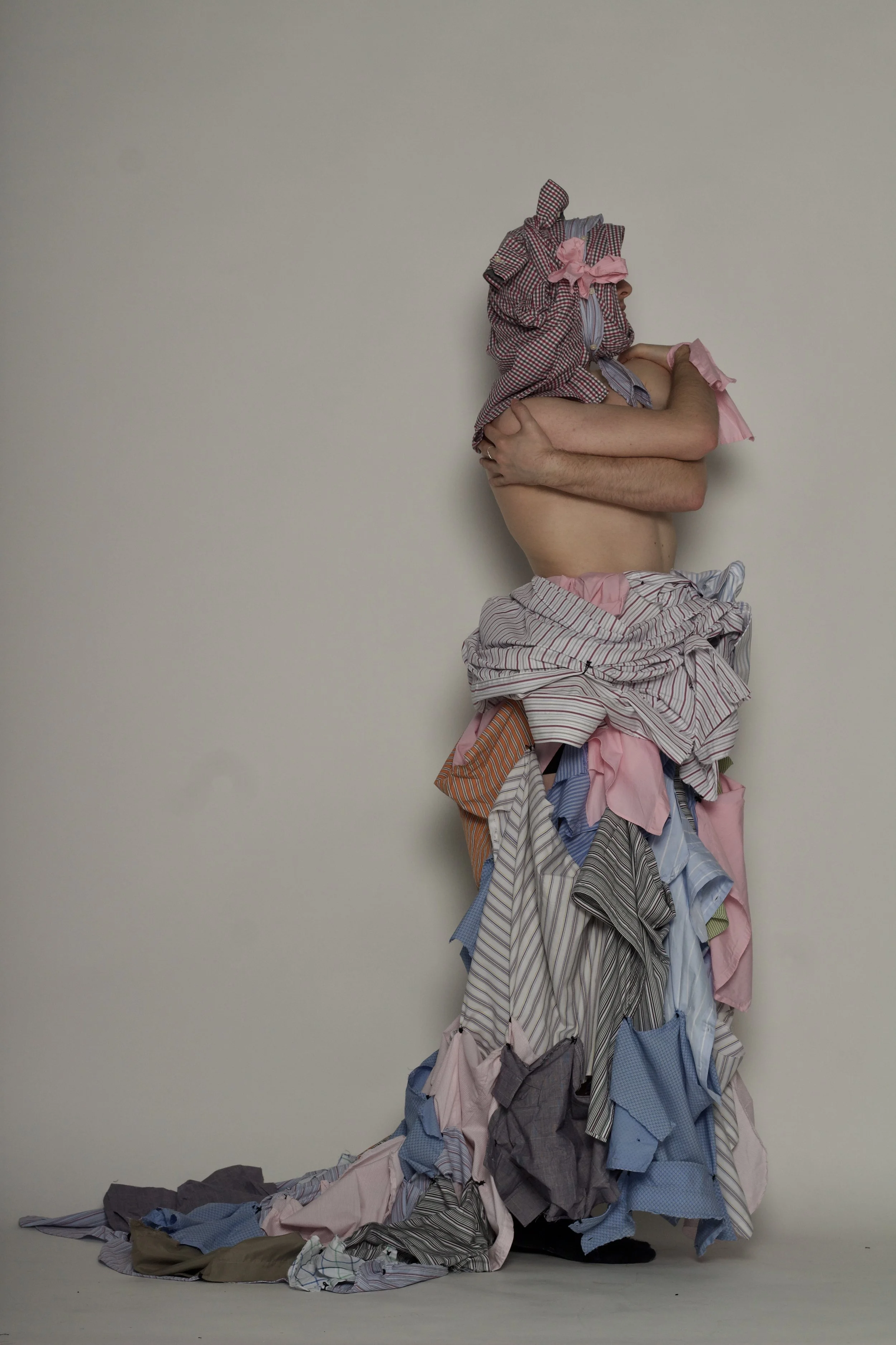 Forma una escultura con ropa arrugada apilada y una persona con ropa en la cabeza en un fondo blanco.