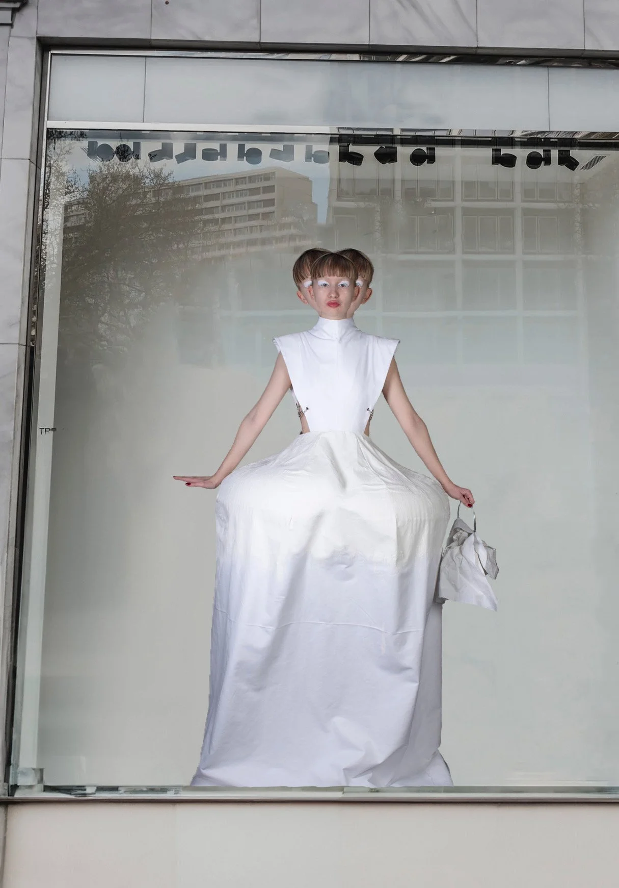 Un escaparate con un cartel de una mujer en vestido largo y blusa blanca, con un fondo de edificios y árboles, y texto reflejado en la parte superior.