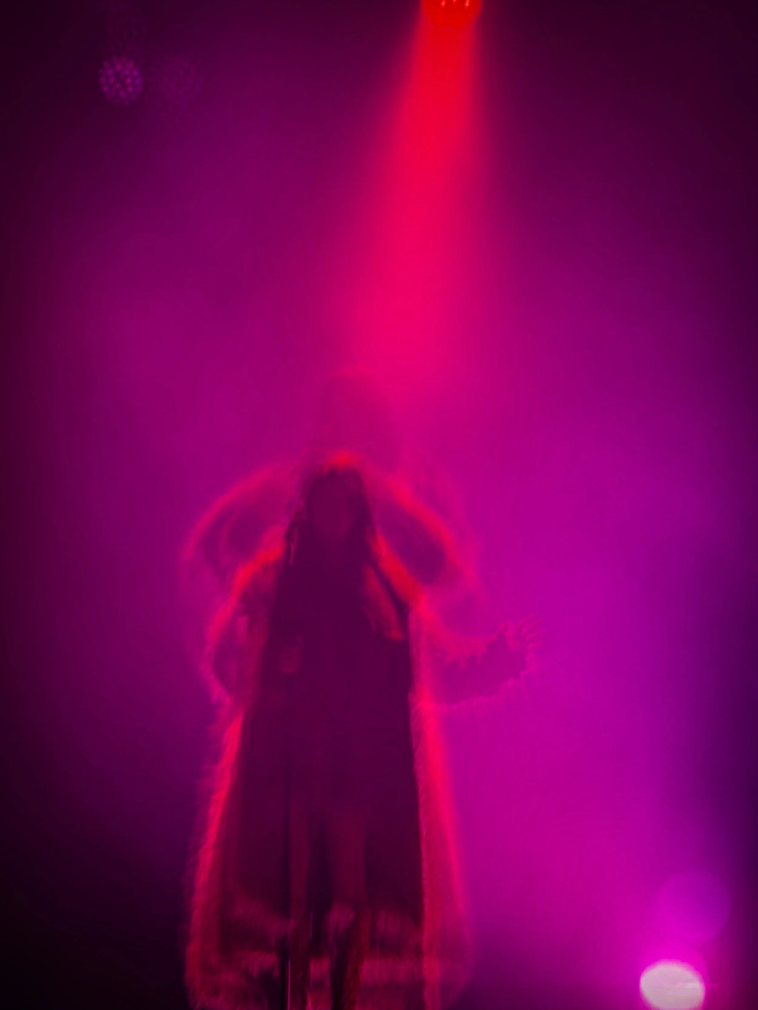 Figura humana de espaldas, en un entorno oscuro con luces moradas y rosas, con un efecto de neón y luz suave.