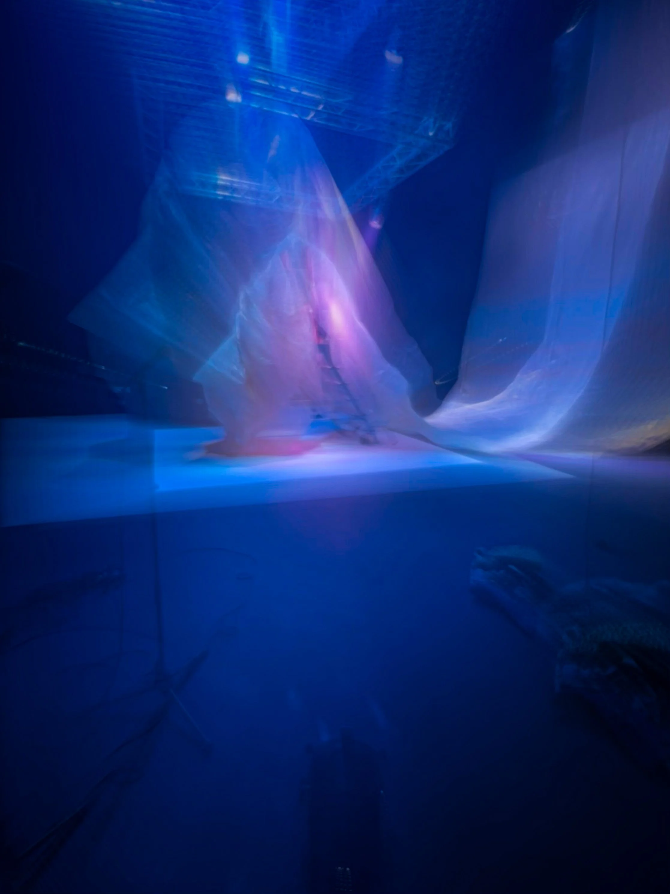 Una escena con formas y luces azuladas, blancas y violetas, que parecen reflejarse en un espacio oscuro y amplio, con efectos visuales de luz y movimiento, en una especie de instalación artística o de un entorno futurista.
