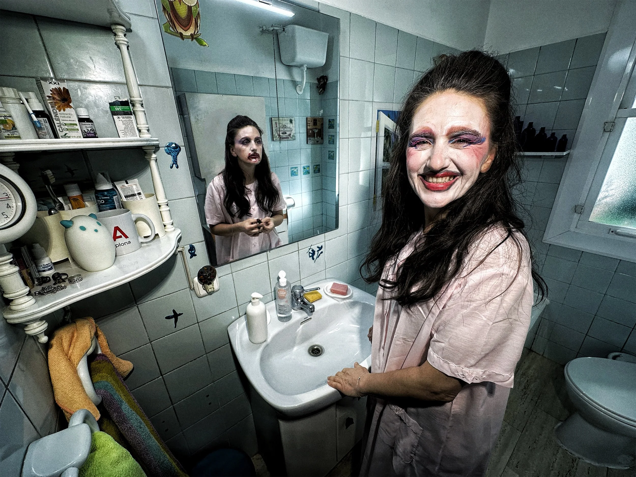 Mujer con maquillaje exagerado y sonrisa en un baño, frente a un espejo, con figuras decorativas y artículos de aseo en las repisas.