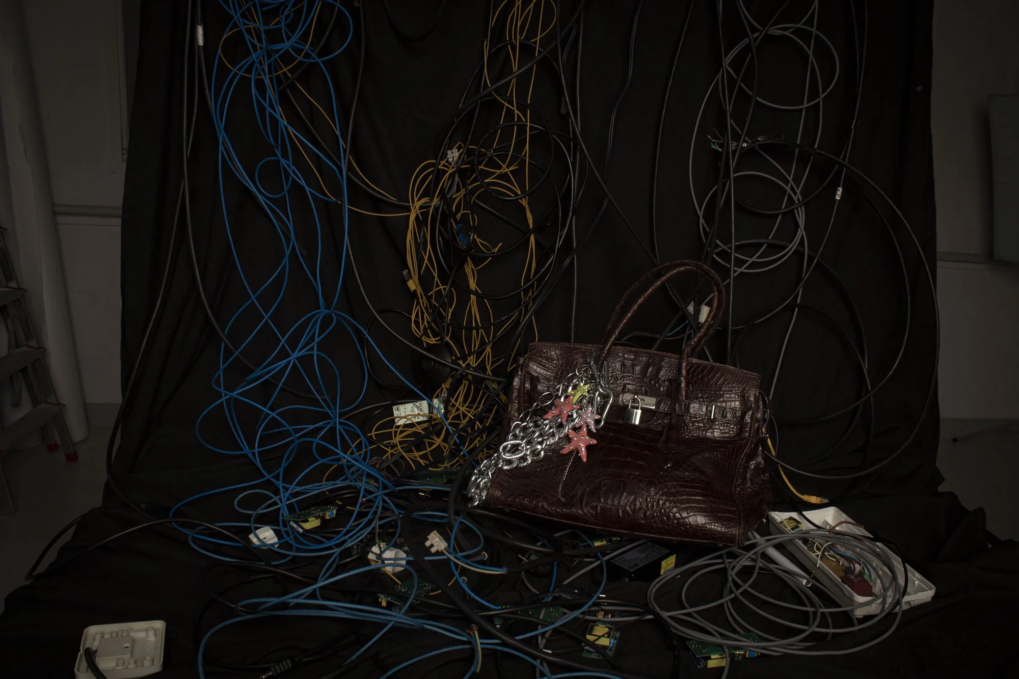 Mesas con una gran cantidad de cables de diferentes colores y una bolsa de cuero con llaveros. En la parte inferior hay una caja blanca de conexiones eléctricas y varias fuentes de poder.