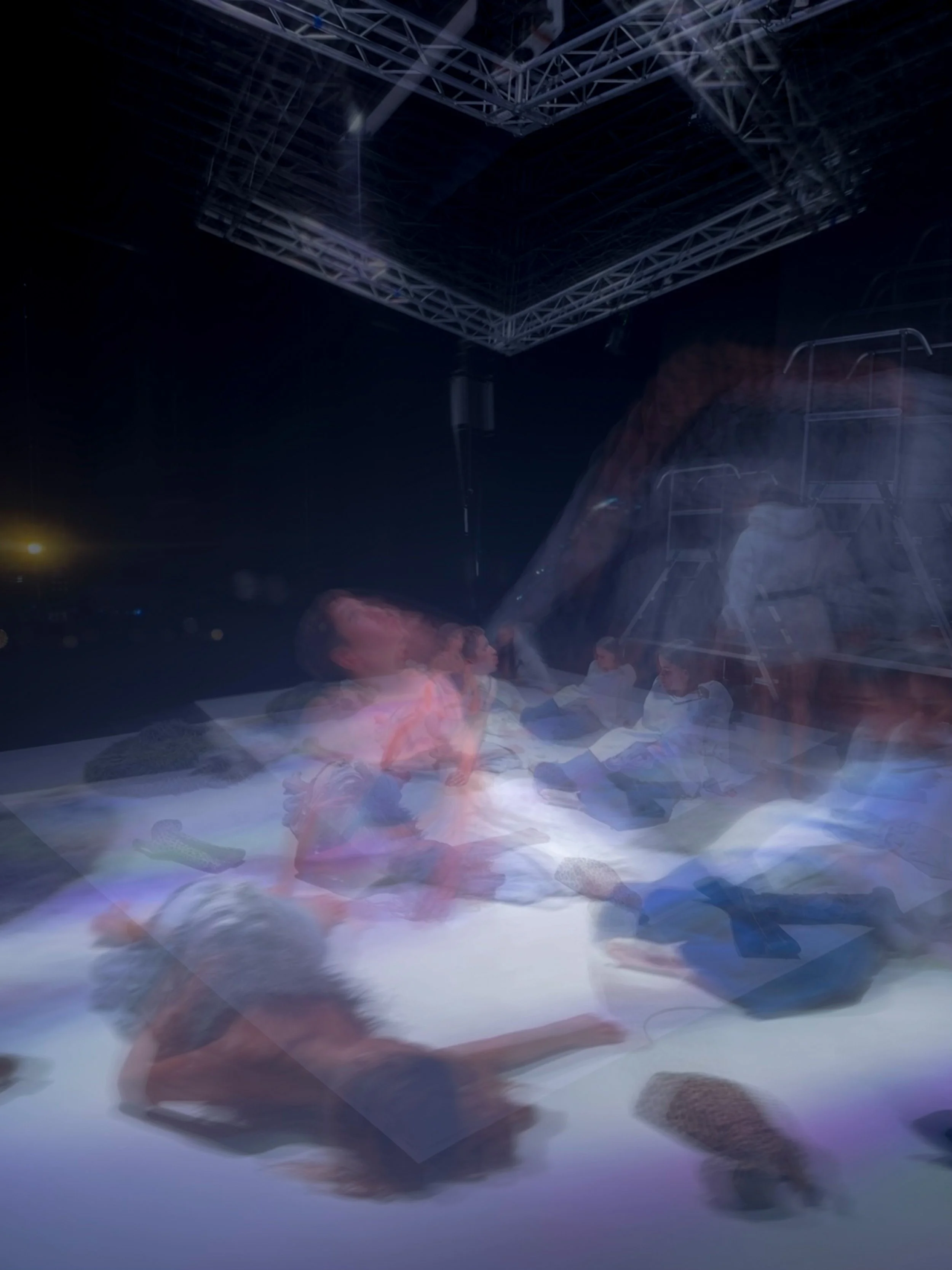 Personas en un escenario con estructura metálica y luces, participando en una actividad nocturna en un espacio abierto.
