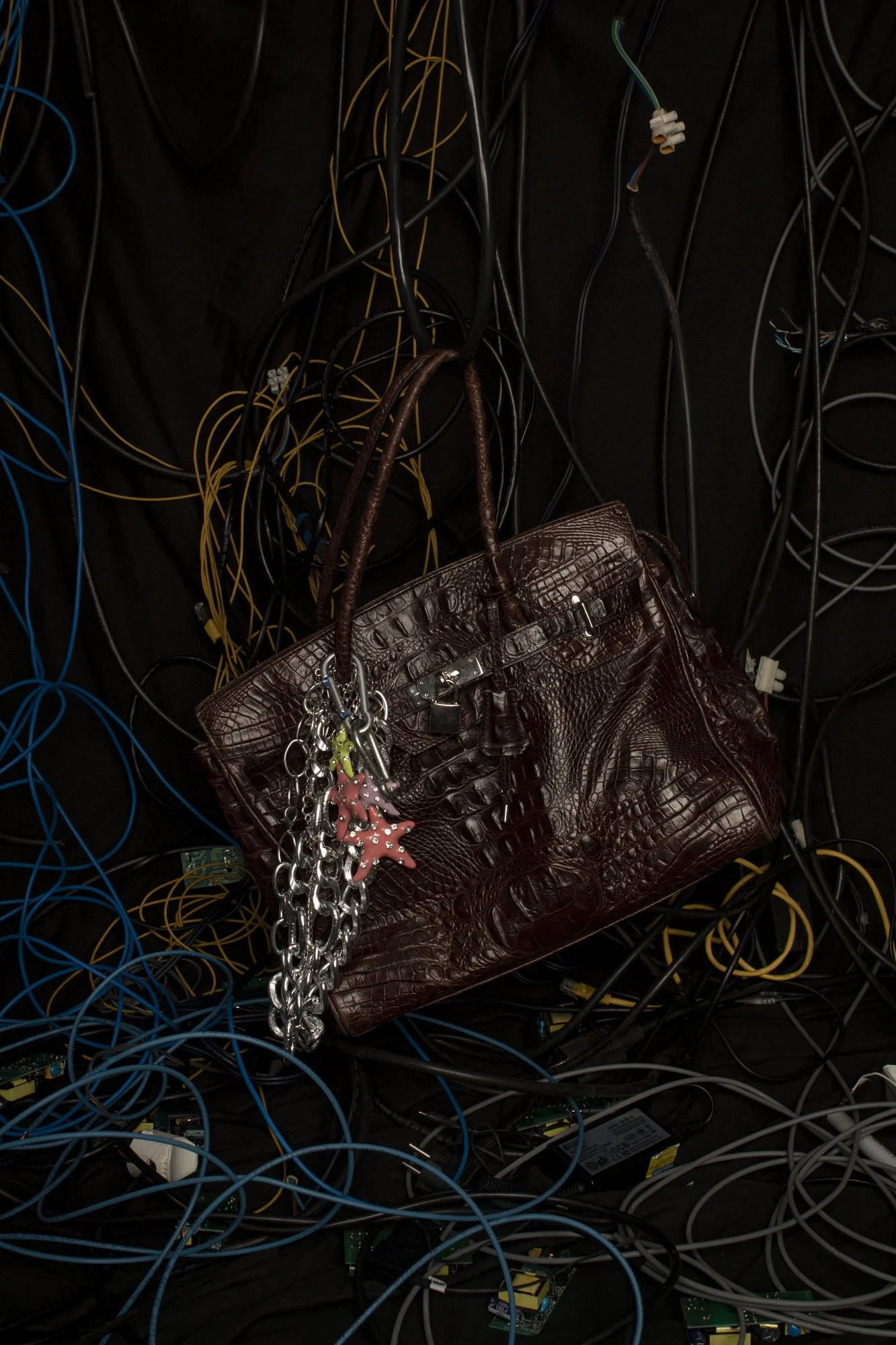 Bolso de cuero marrón con cerradura, colgado entre cables de diferentes colores en una superficie negra.