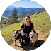 Person hiking with a backpack on a mountain trail with a lake and mountains in the background.