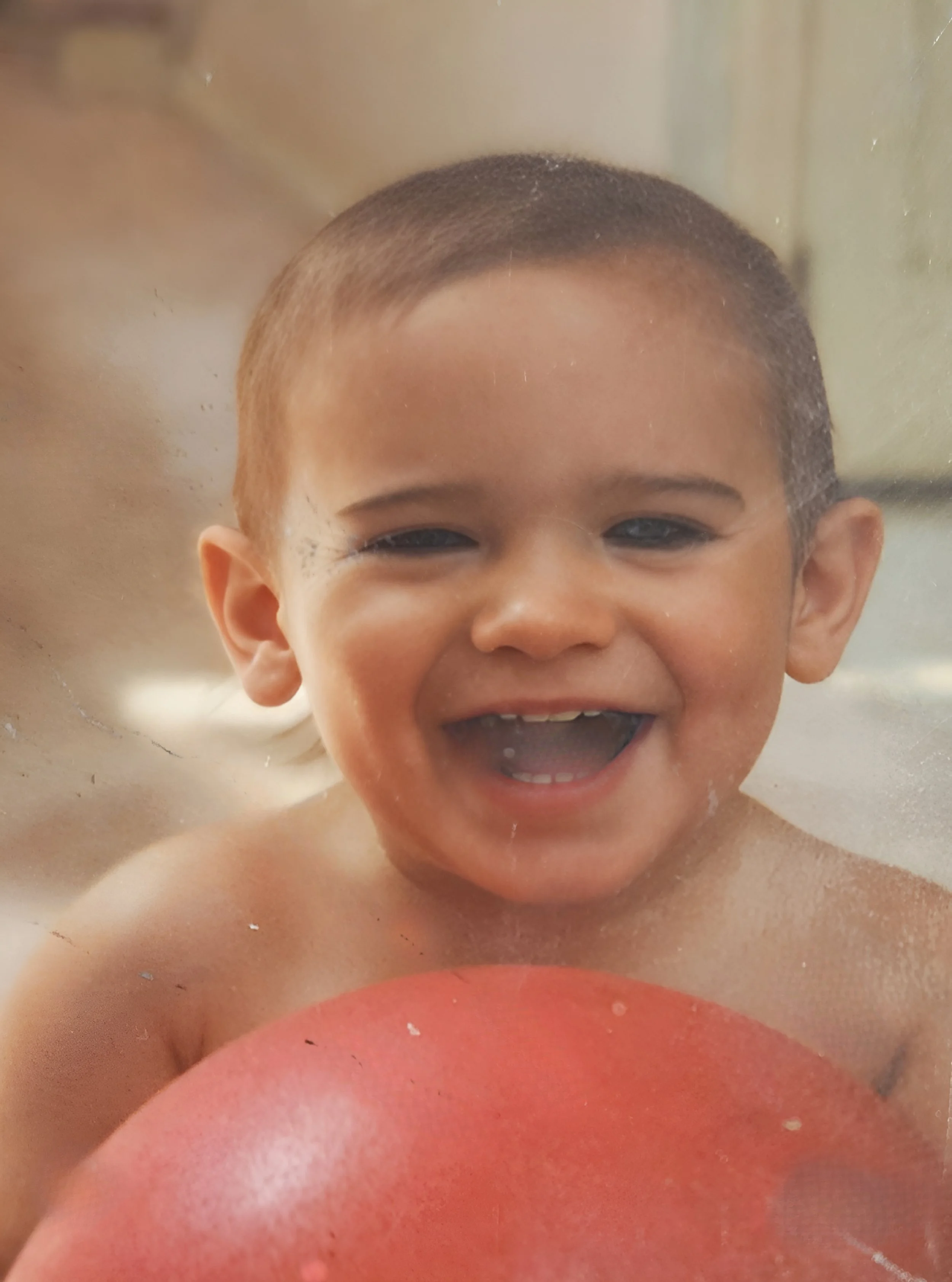 A young boy with a big smile, in a bathtub, holding a red ball.