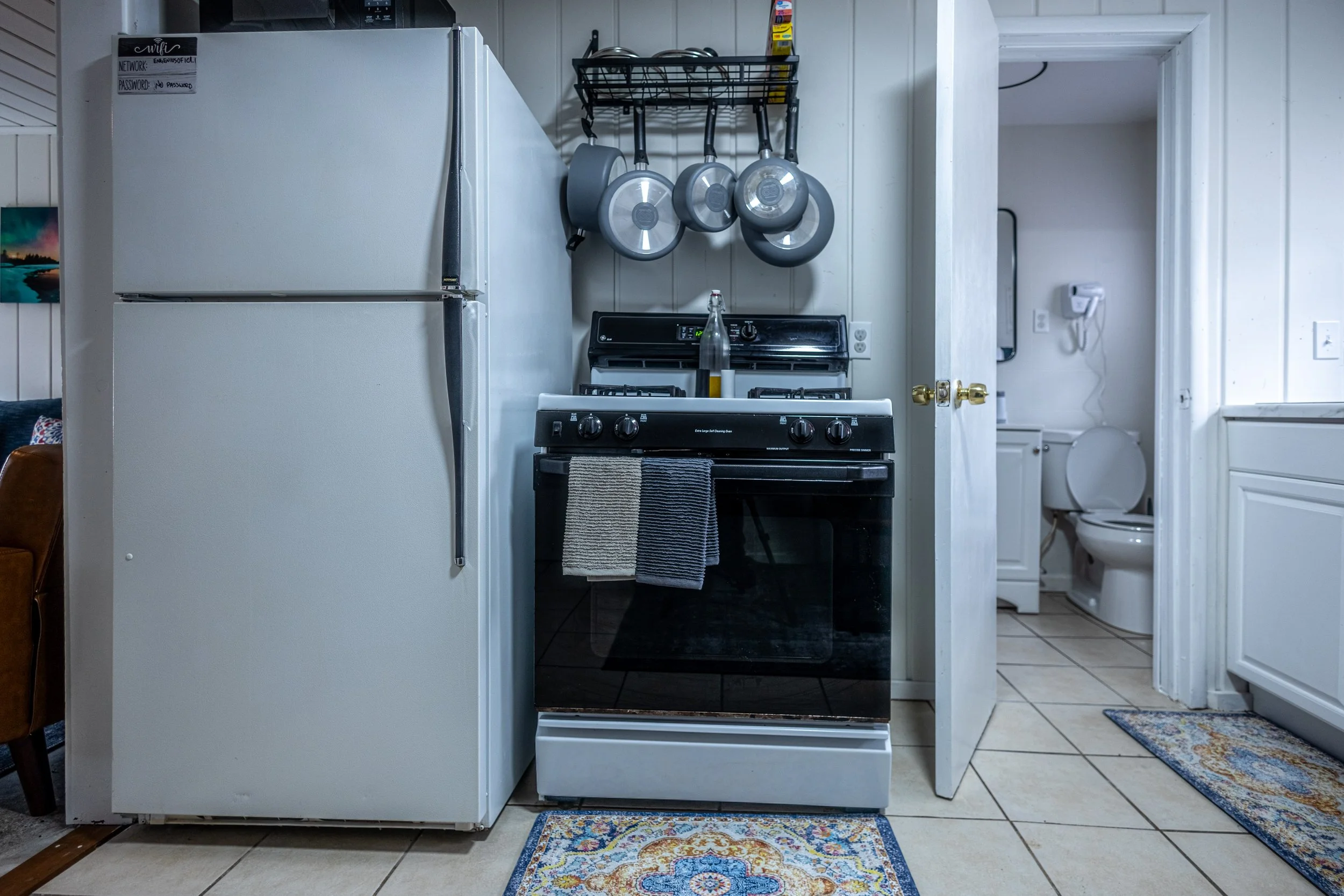 Kitchen with refrigerator, stove, and a small bathroom with a toilet visible through an open door.