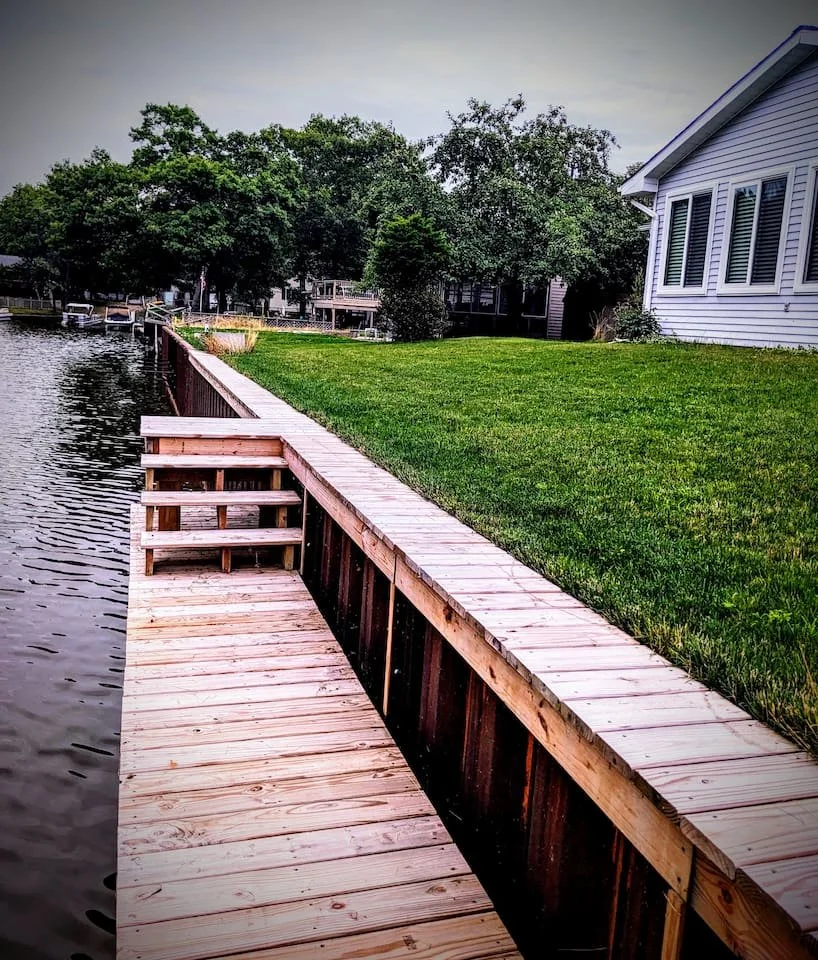 A backyard with a wooden dock extending over a canal leading to Lake Huron, green grass, trees, and The Canal House.