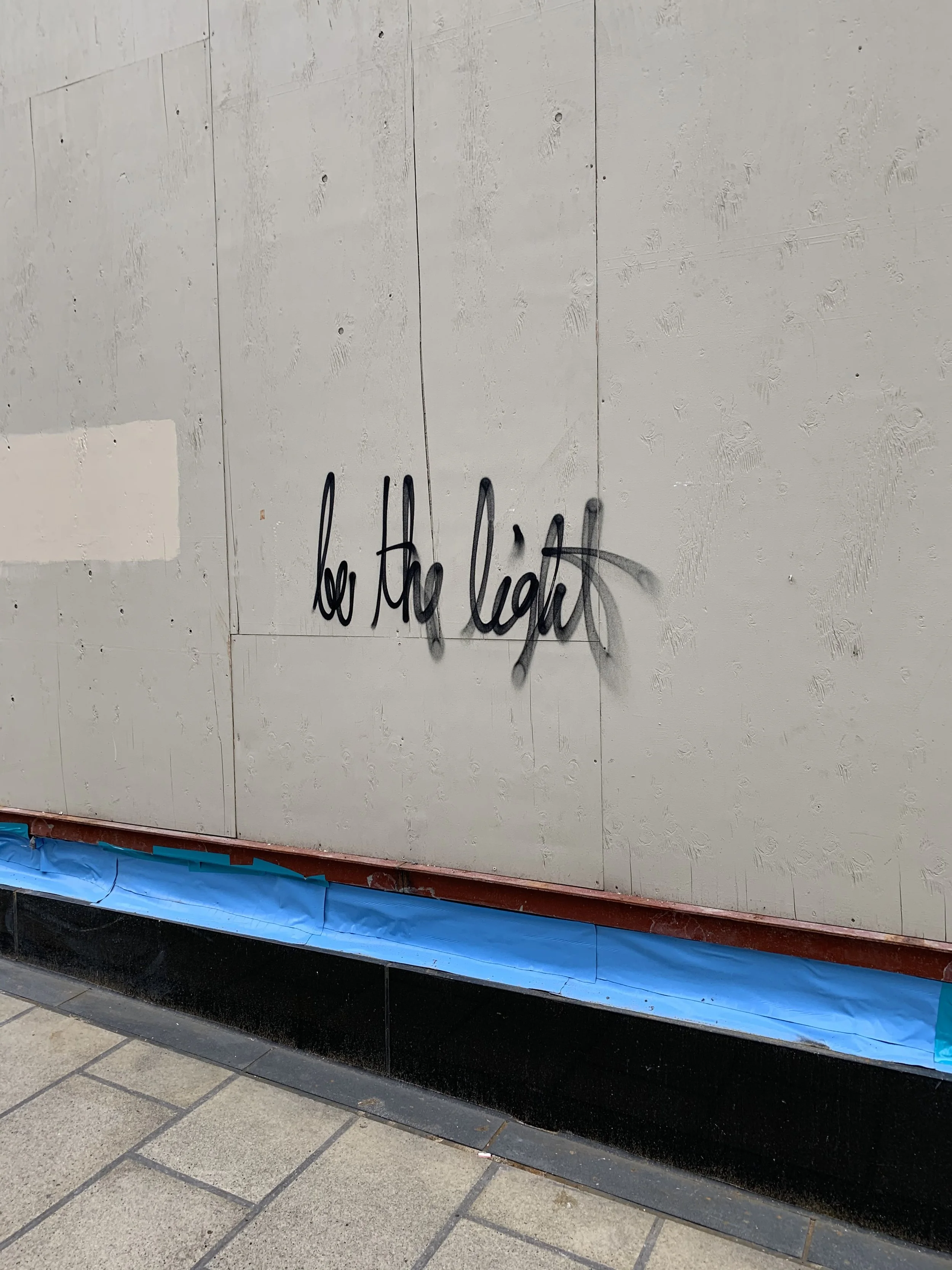 Graffiti on a wall that reads 'be the light' with shadows cast by the spray paint.