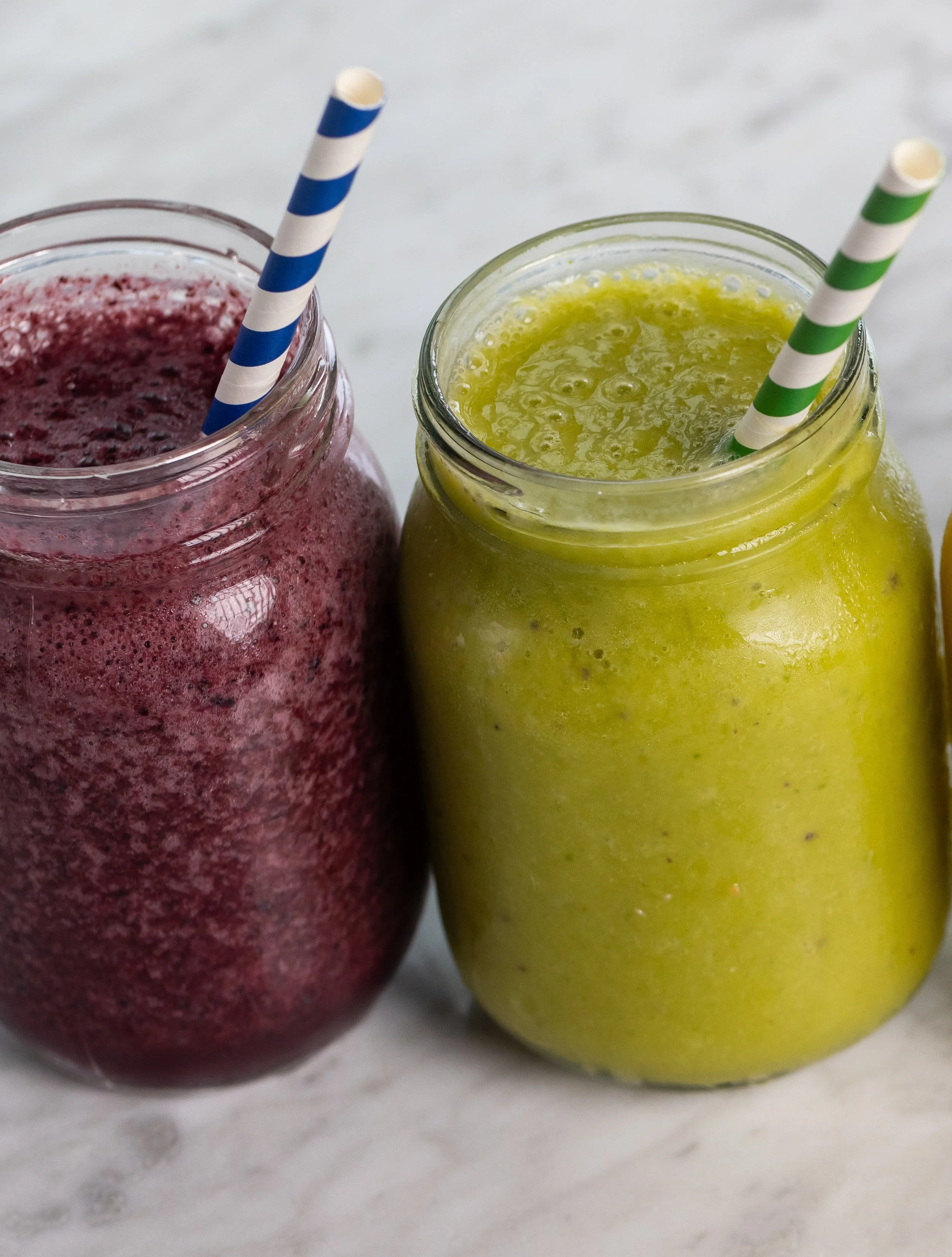 A purple smoothie and a green smoothie, both in mason jars with colorful paper straws At Fancy Pants Cafe in Bridgewater, Nova Scotia