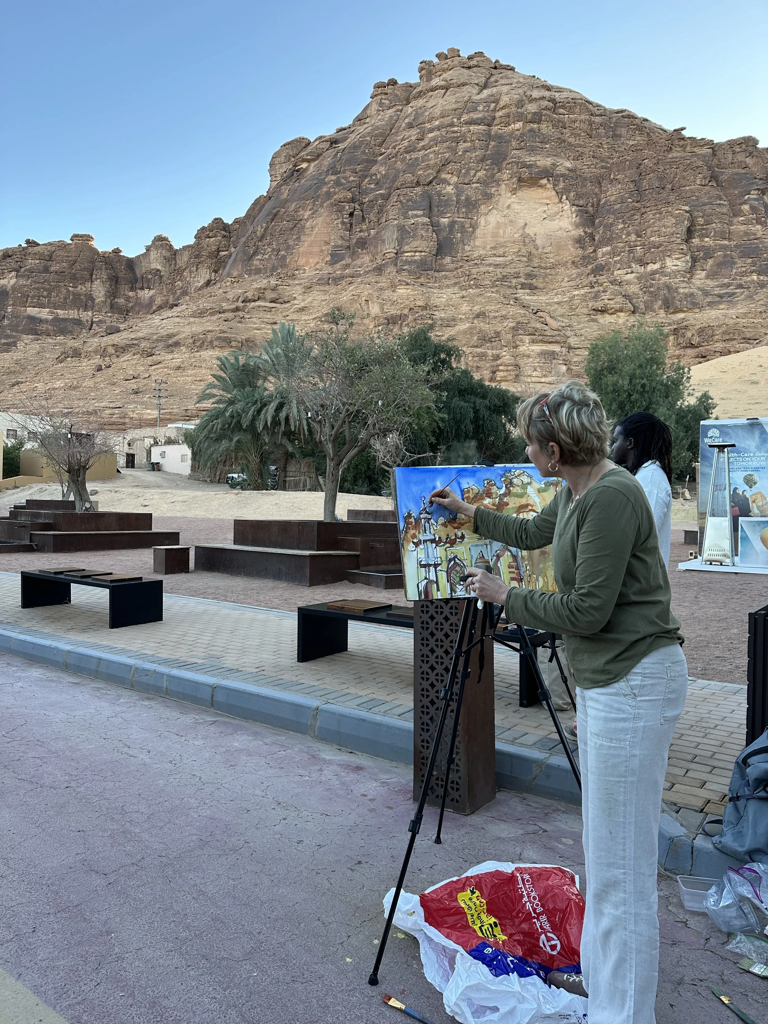 Erin McGee Ferrell painting outdoors on an easel beneath the rock formations of AlUla.