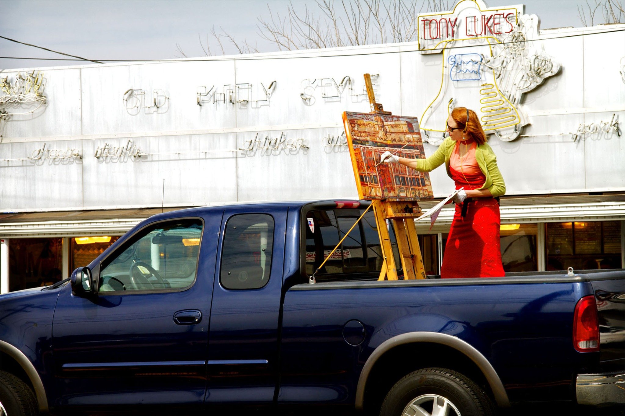 Erin McGee Ferrell painting Tony Luke’s on location in Philadelphia, standing in the bed of a pickup truck with her easel.
