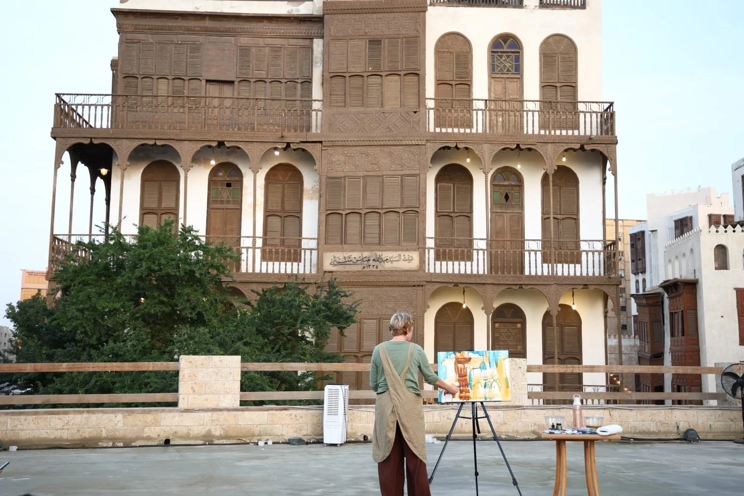 Erin McGee Ferrell painting at an easel in front of a historic building during an outdoor workshop in Jeddah.