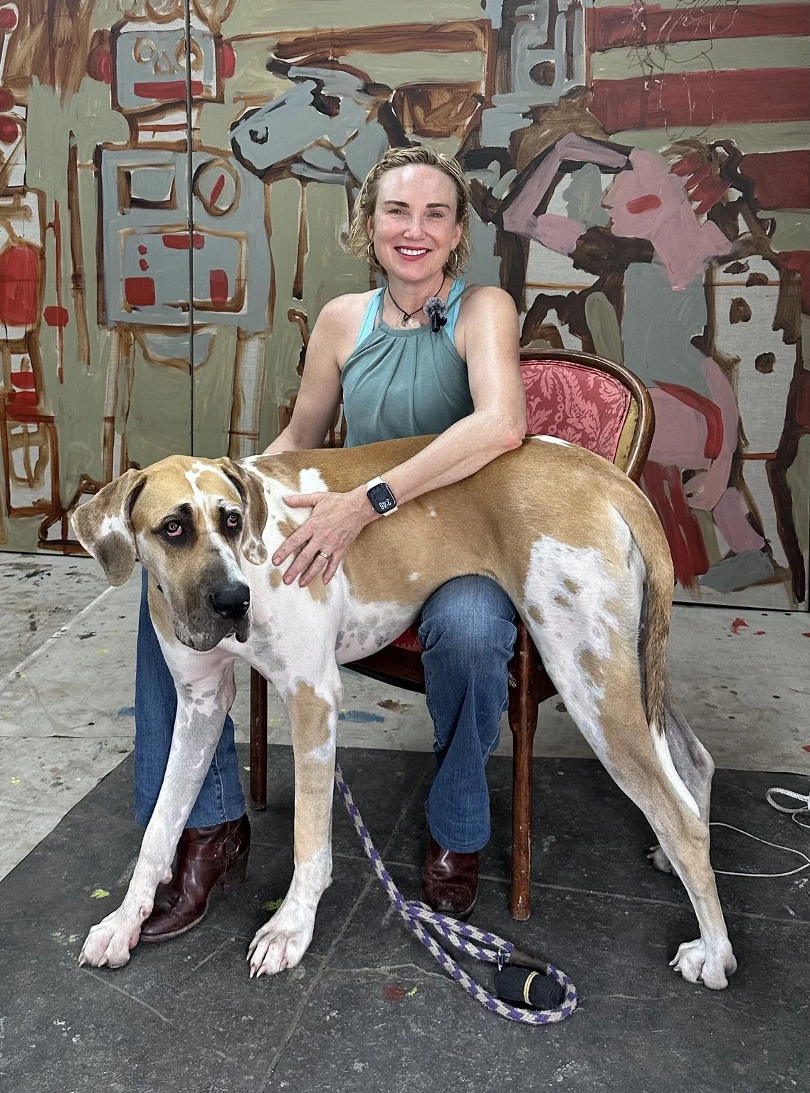 Artist Erin McGee Ferrell seated with her Great Dane, Oona, in her Louisville studio before a large narrative painting.