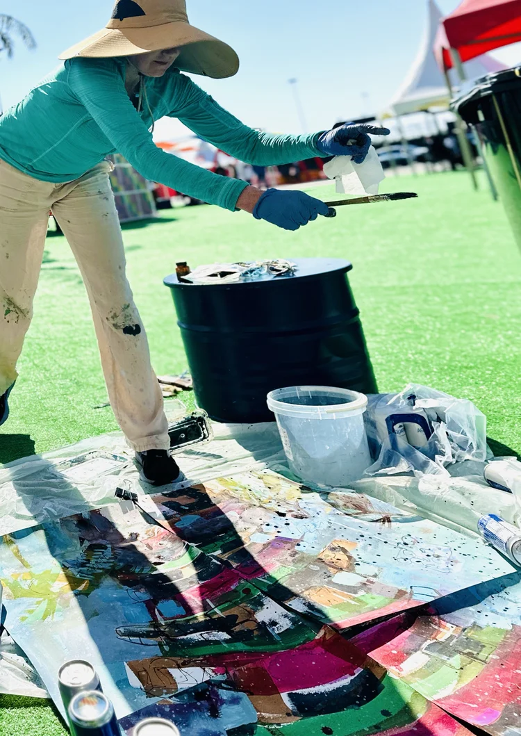 Erin McGee Ferrell applying paint to a large work laid on the ground at the Bahrain Grand Prix.