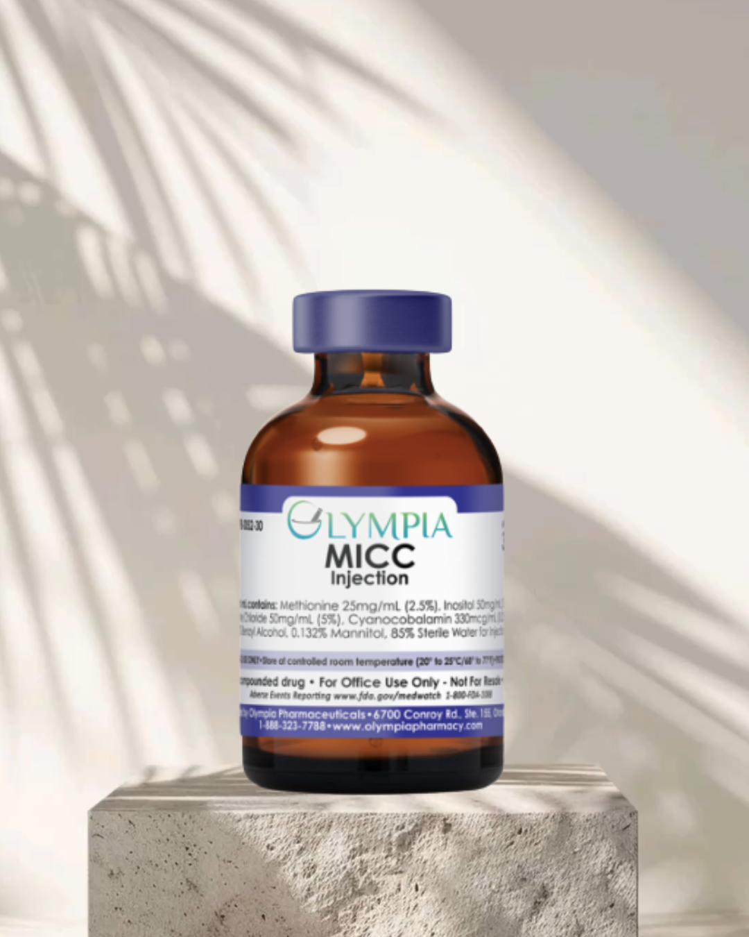 A brown glass vial labeled 'Olympia MICC Injection' with a blue cap, placed on a concrete surface with sunlight and shadow patterns in the background.