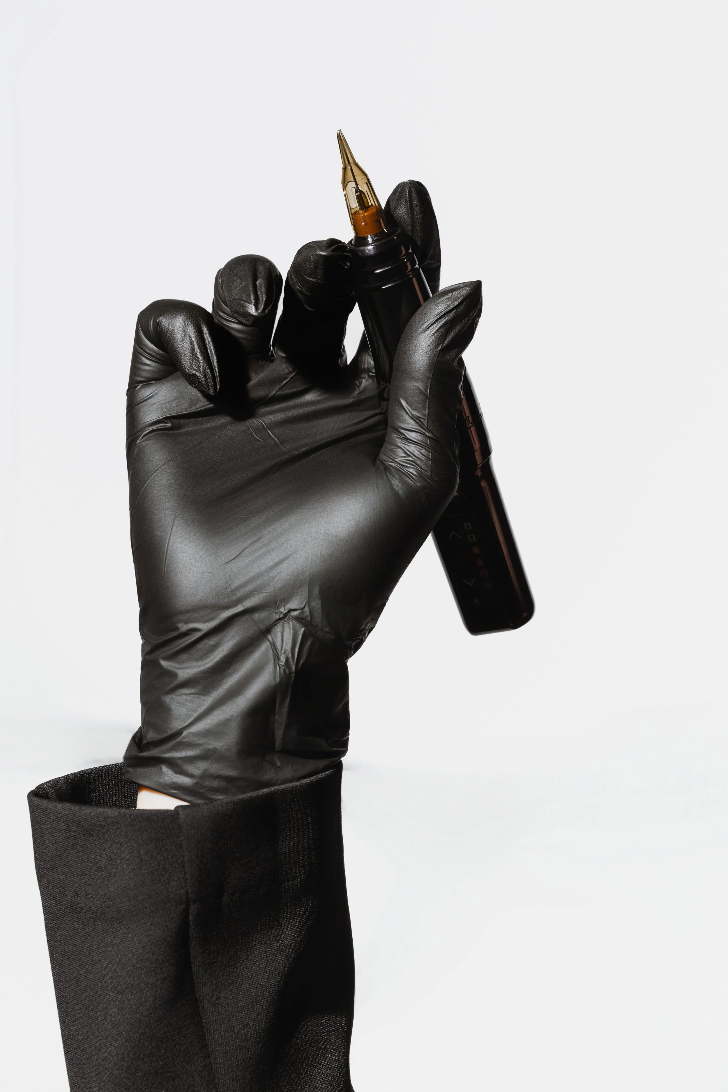 A hand wearing a black glove holding a black marker with a gold tip, with a black sleeve visible.
