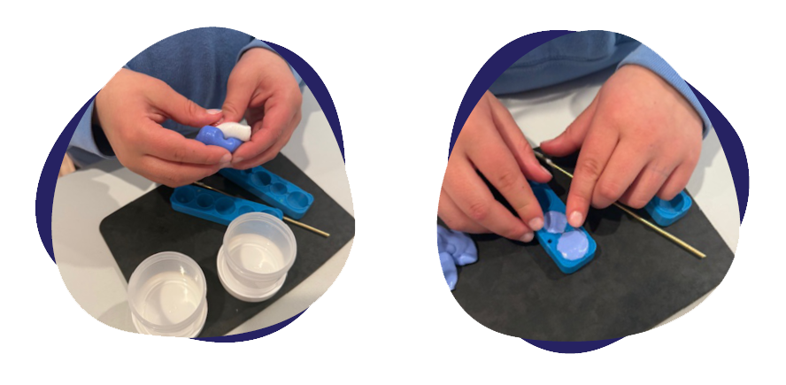 Child using a blue ice cube mold, pouring water into it with a small container, preparing to freeze ice, on a black surface.