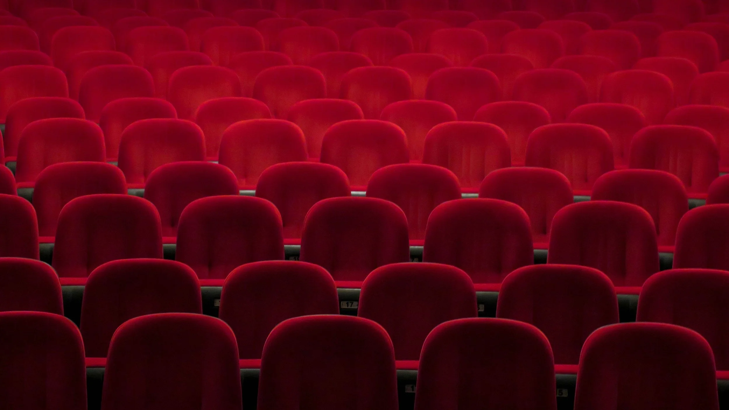 Empty rows of red theater or cinema chairs in a darkened auditorium