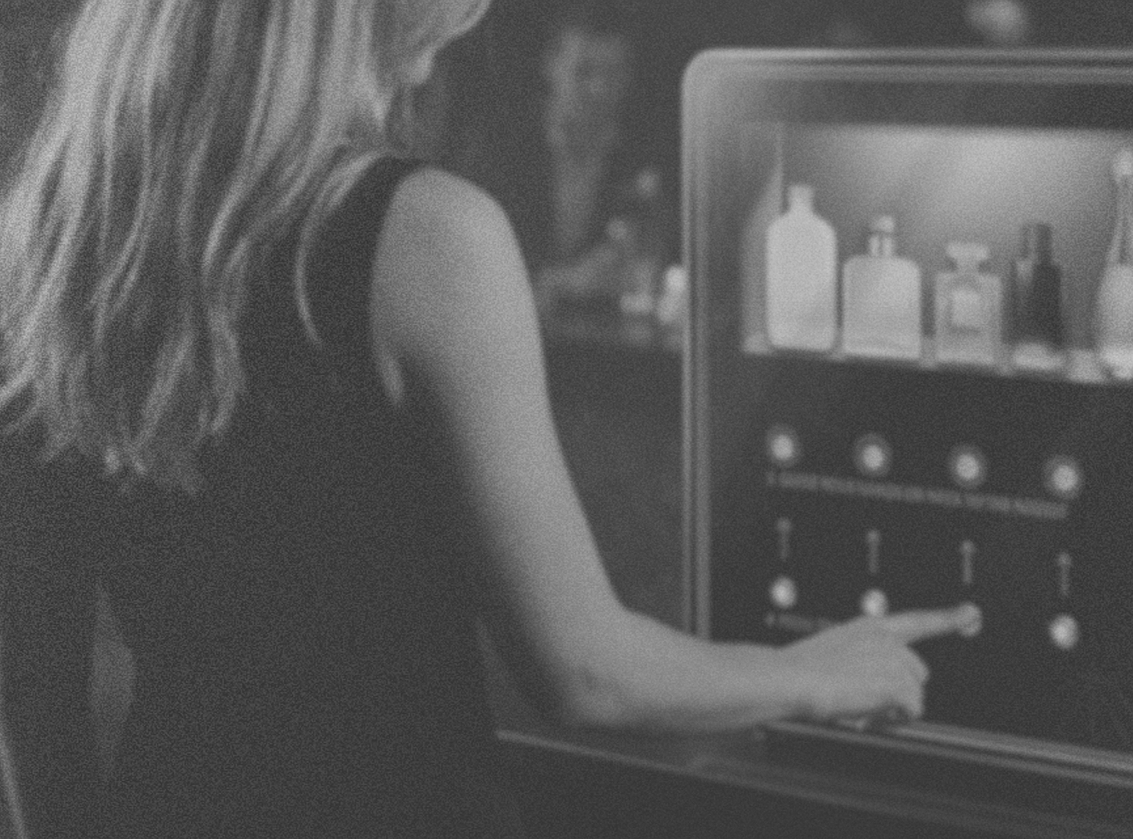 A person with long hair pointing at a keypad on an arcade game machine.
