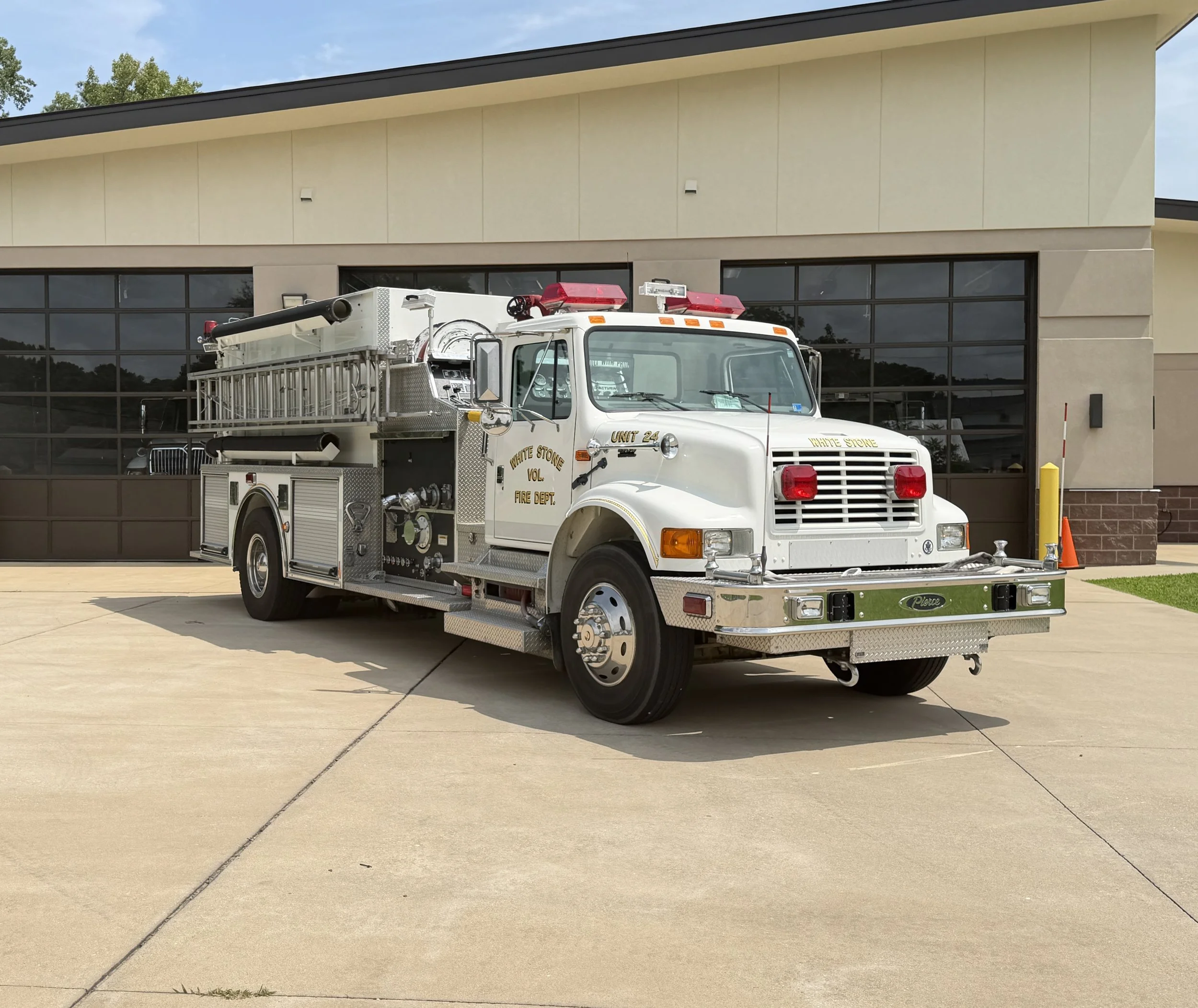 A white fire truck parked outside a modern building with large glass windows and beige walls.