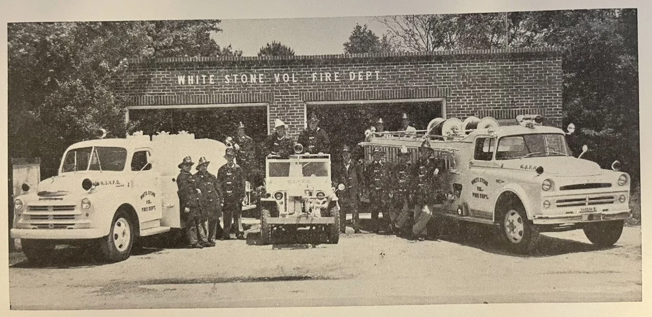 Black and white photo of firefighters in front of a brick fire station labeled "White Stone Vol. Fire Dept." with fire trucks and equipment, and trees in the background.