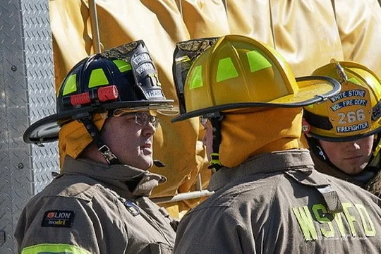 Firefighters in gear wearing yellow helmets and protective uniforms engaged in a discussion.