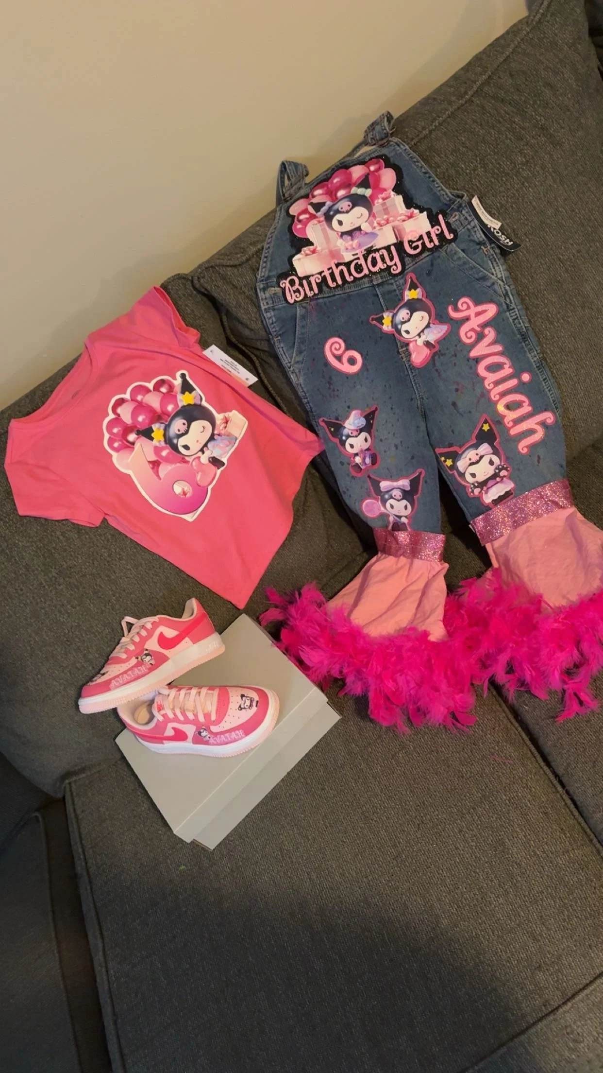 Birthday girl's themed clothing and accessories on a couch, including a pink T-shirt, a pair of pink Nike sneakers, and a denim jacket with birthday decorations, featuring characters with balloons, pink feathers, and custom text.