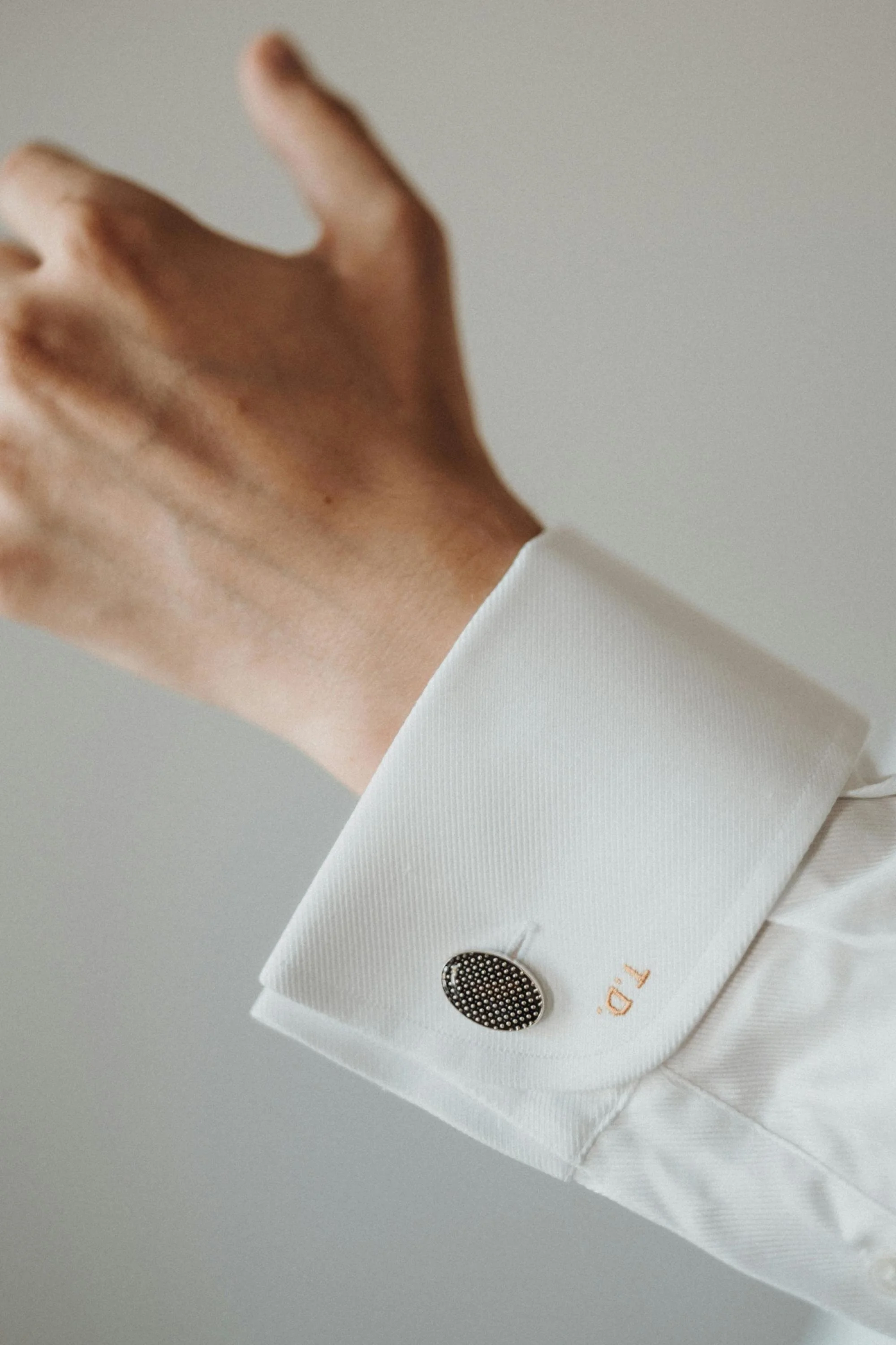 Close-up of a white dress shirt cuff with a black and gold oval cufflink and the initials 'T.D.' embroidered in orange.