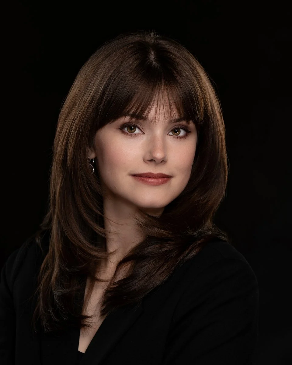 Portrait of studio director with brown hair wearing a black top, against a dark background.