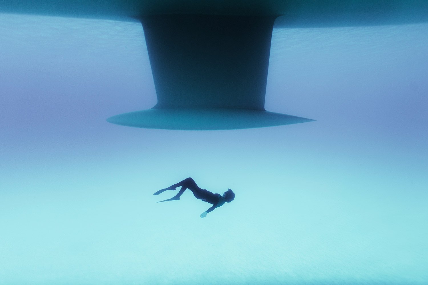 A person in a wetsuit swimming underwater beneath a large ship hull.