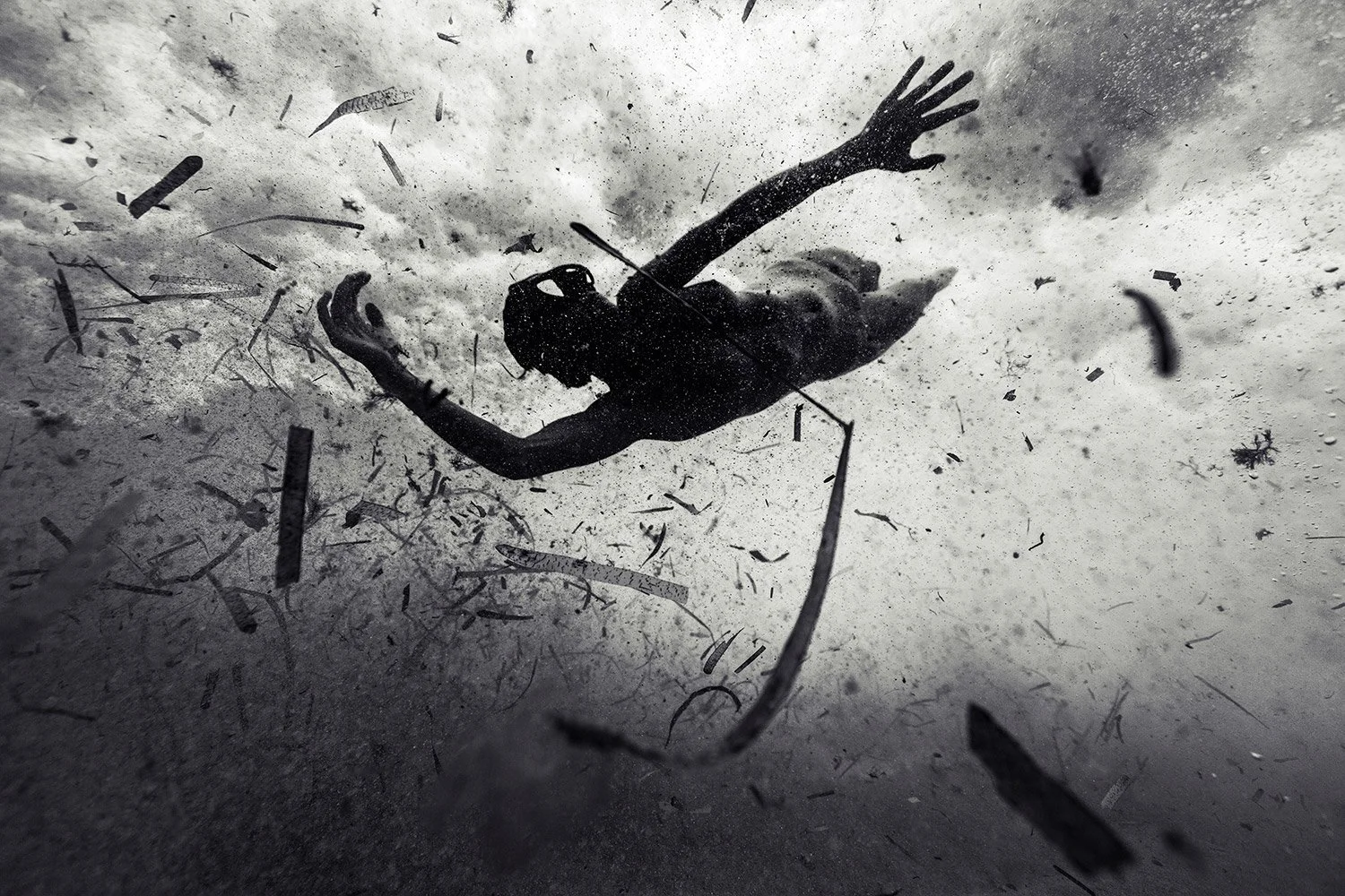 A person in scuba diving gear swimming underwater among debris and particles in the water.