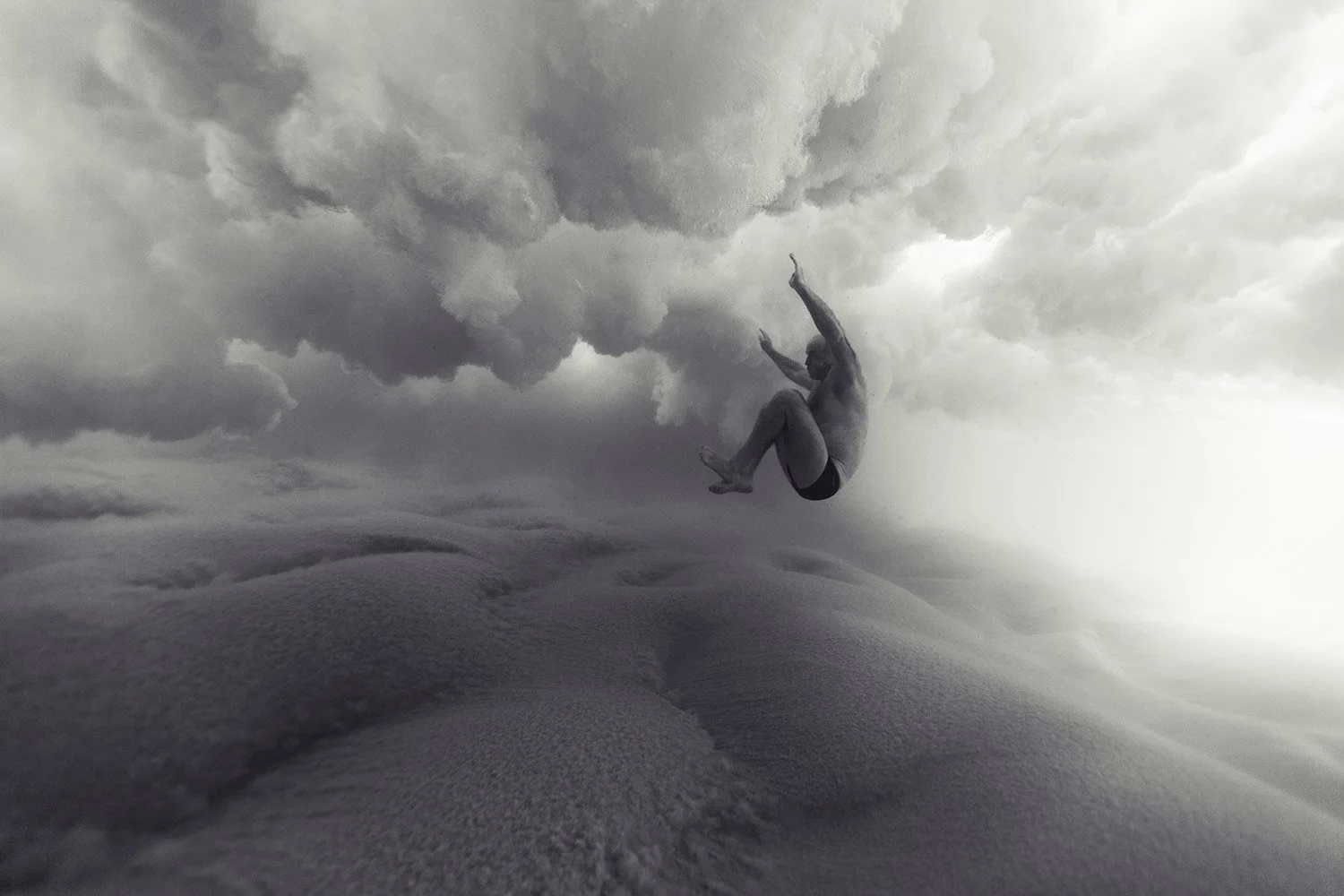 Black and white photo of a person mid-air, falling or jumping, with cloudy sky background.