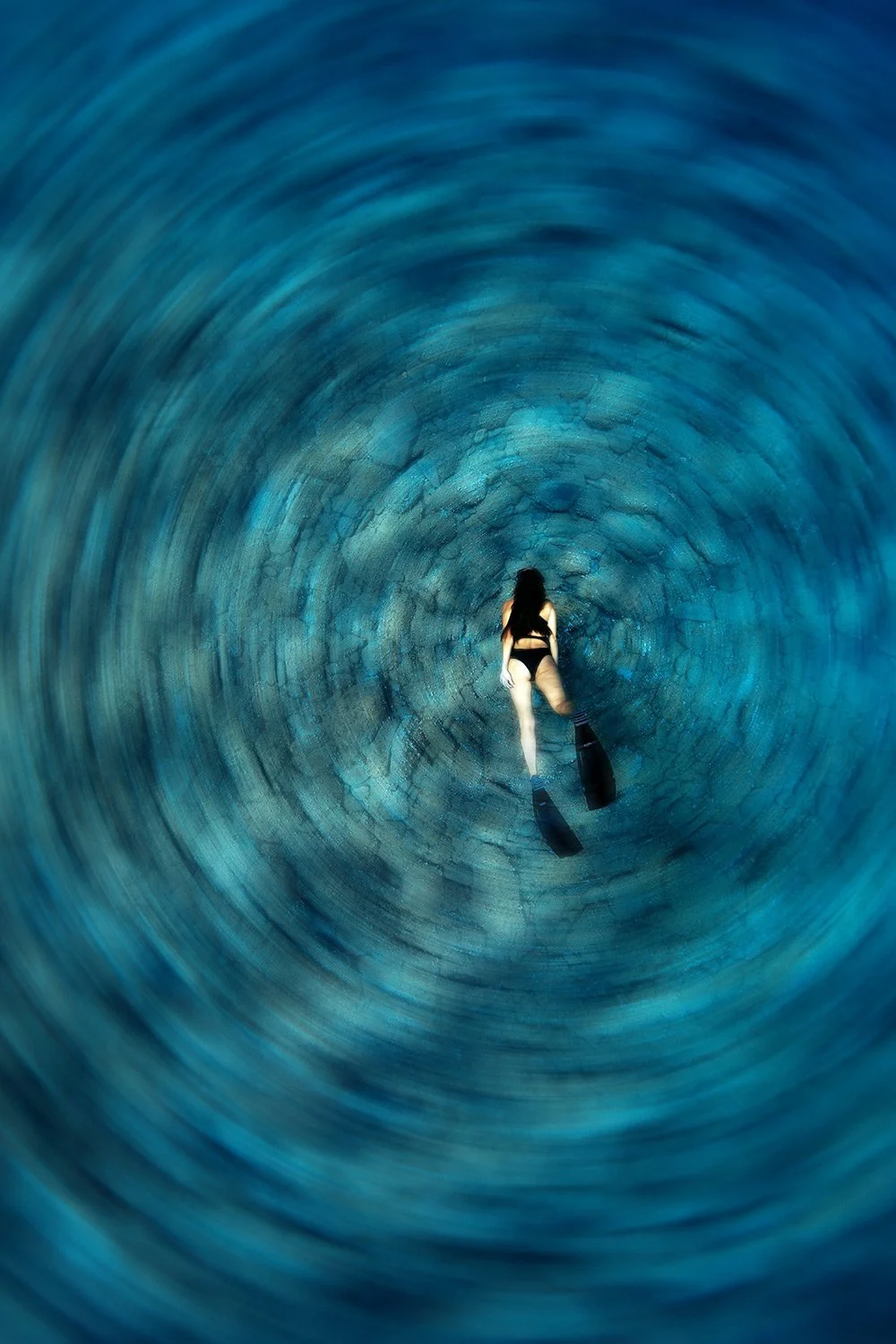 A person in swimwear with fins snorkeling inside a circular underwater tunnel.