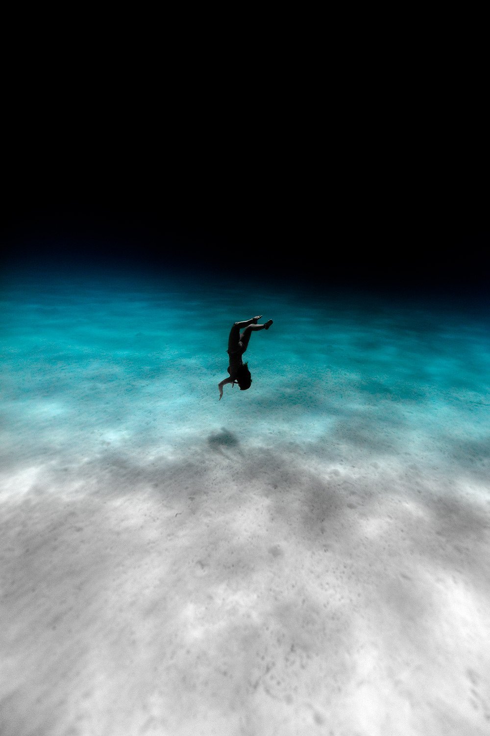 A person falling upside down into the water of an ocean or sea at night, with the dark sky above.