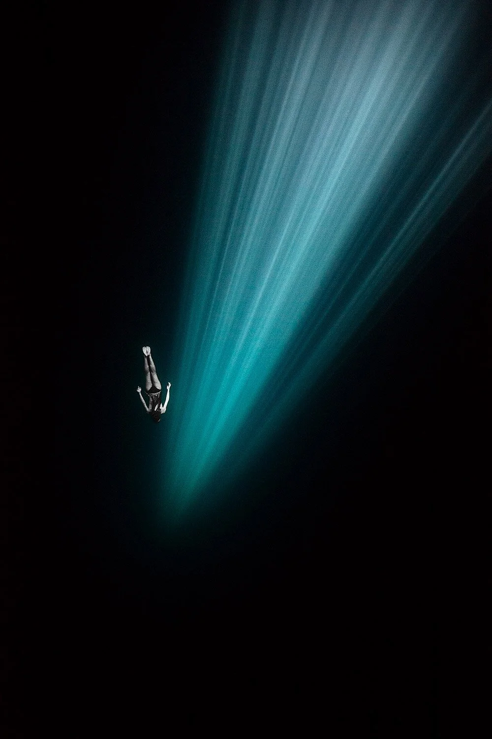 A person free-falling through a dark night sky with a beam of blue light behind them.
