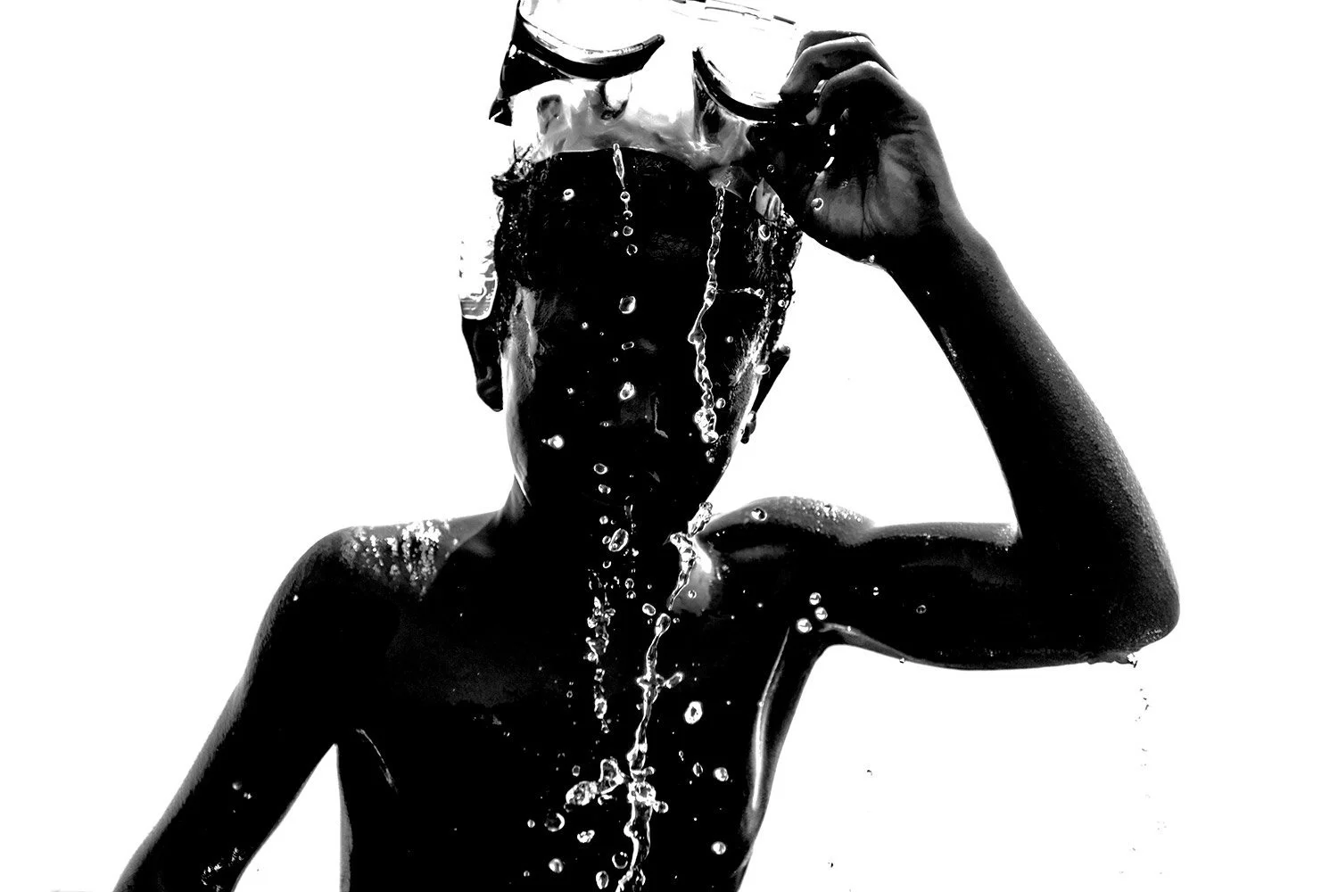 Black and white photo of a person holding sunglasses, with water splashing on their face and body.