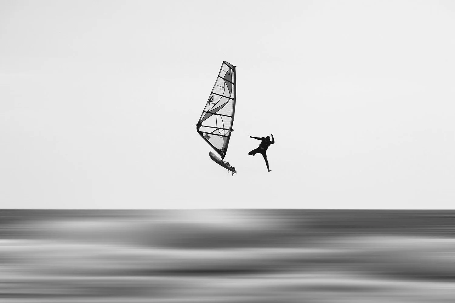 Silhouette of a windsurfer performing a jump above the water with a clear sky in the background, black and white image.