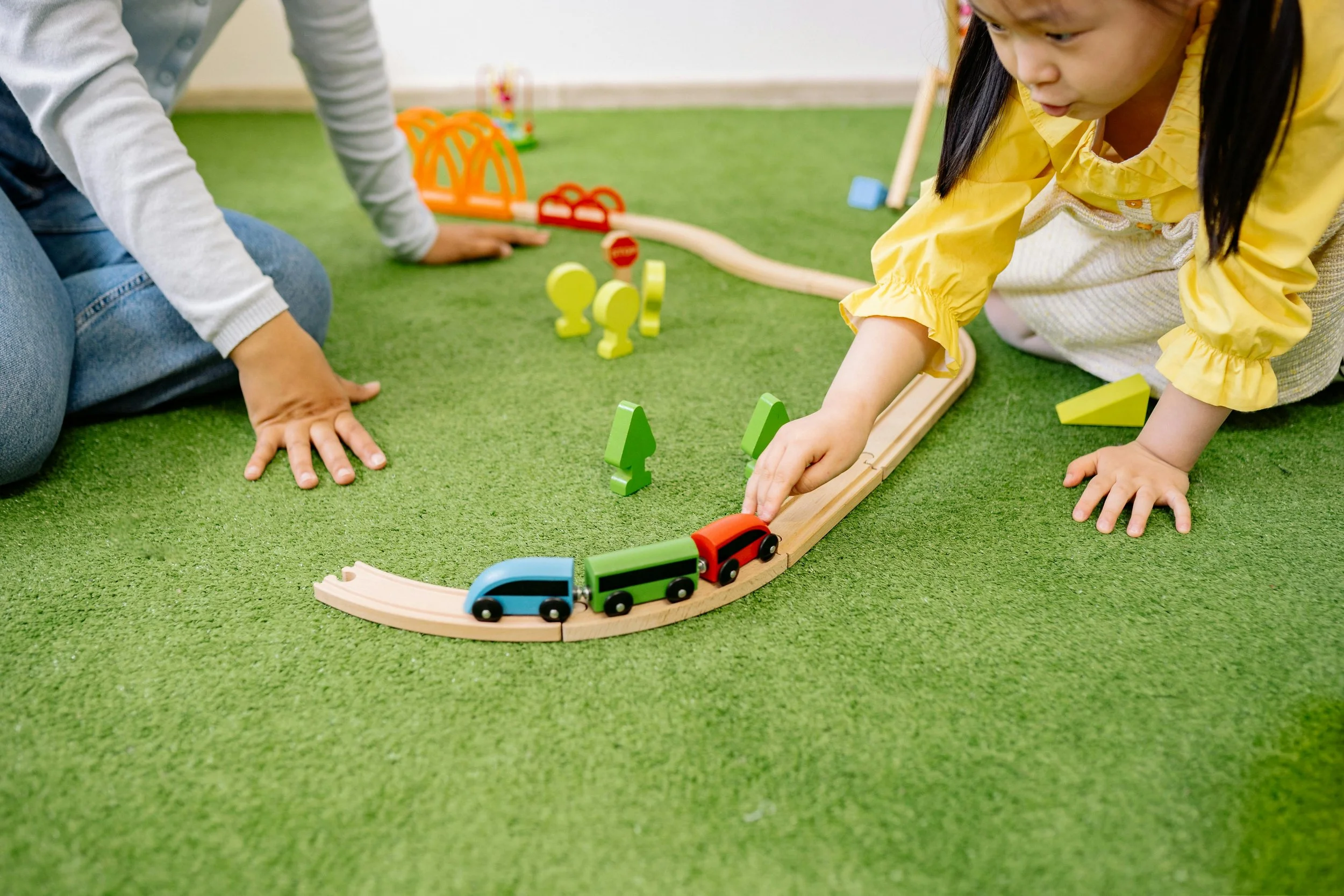 Children playing with a toy train set on a green carpet.