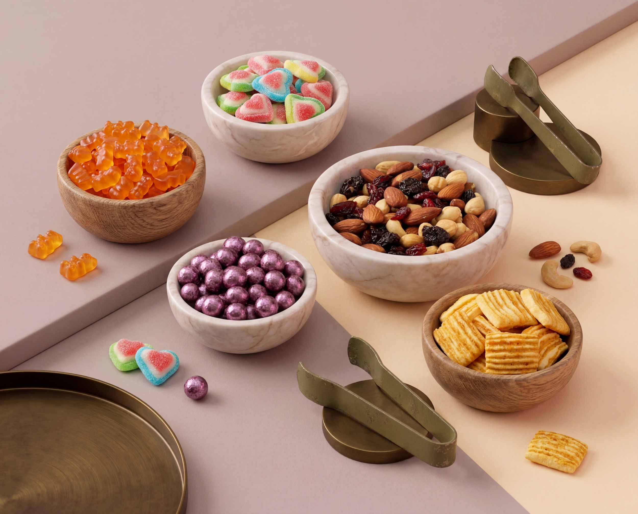Assorted candies and nuts in bowls on a table with metal tongs and a round metal tray.