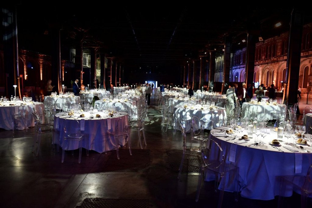 Sala da ricevimento elegante con tavoli rotondi con tovaglie bianche, apparecchiature da tavola e luci soffuse, in attesa di ospiti.