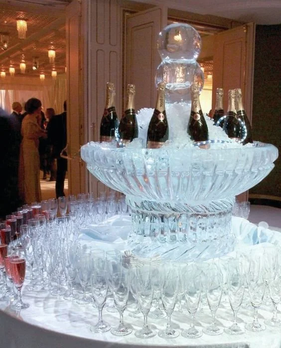 Fontana di cristallo decorata con bottiglie di champagne e sfera di ghiaccio in un evento elegante.