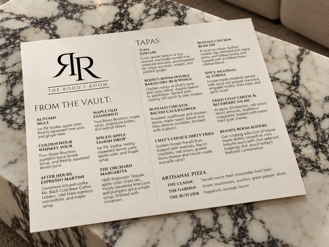 A restaurant menu titled 'The Rood's Room' is placed on a marble table. The menu features sections for 'From the Vault' and 'Tapas,' listing various food and drink options with descriptions.