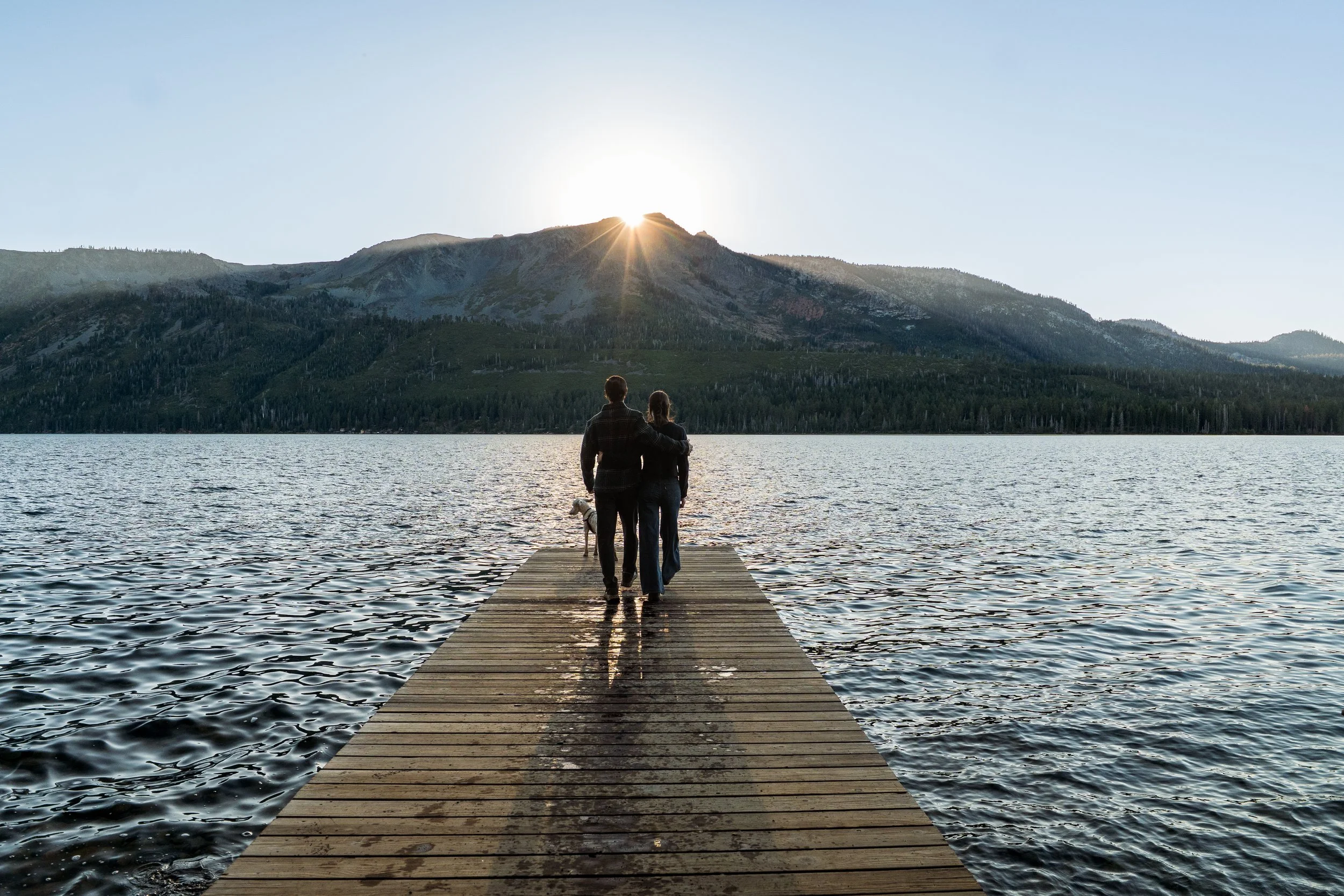 Couple walking to the end of a dock on Fallen Leaf Lake with their dog at golden hour