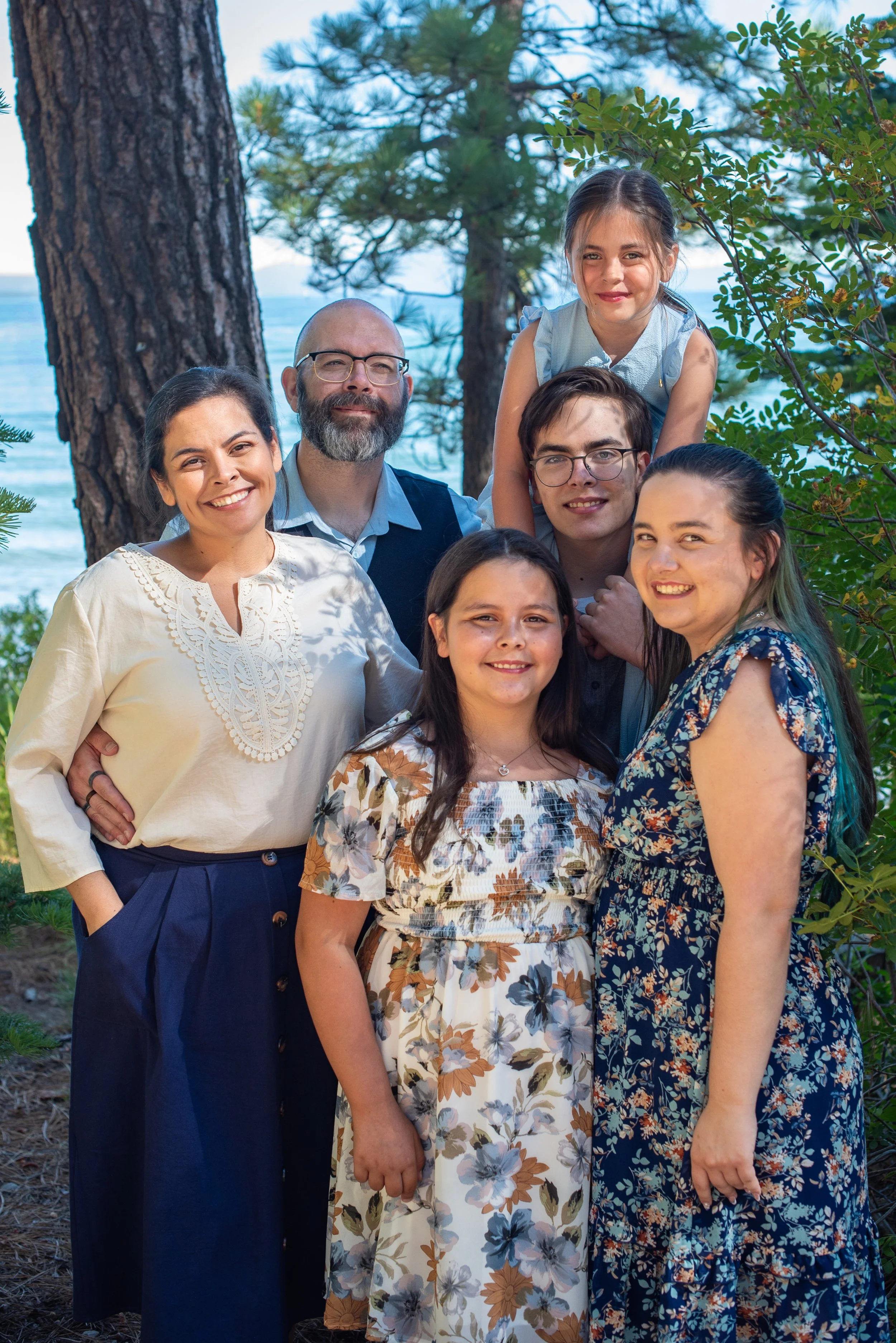 Family of six smiling in the pine trees with the lake in the background