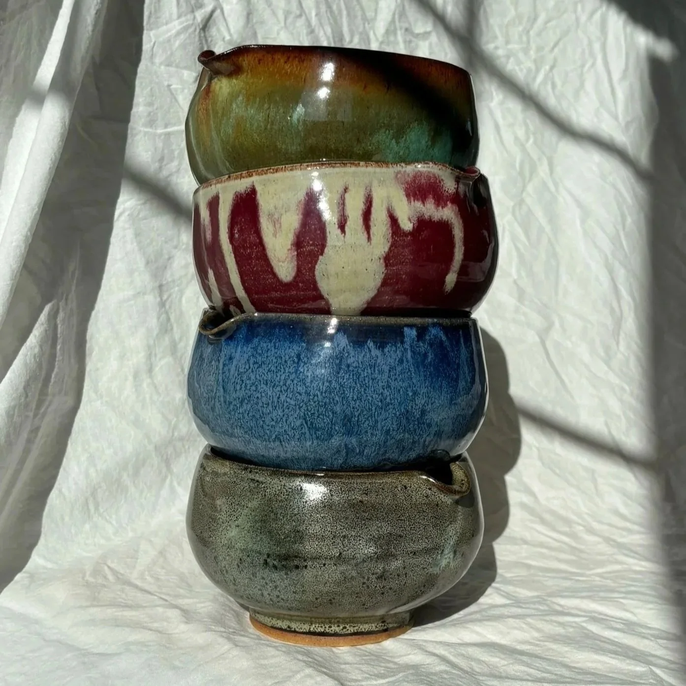 Stacked matcha bowls with various glaze colors on a white textured surface with shadows.