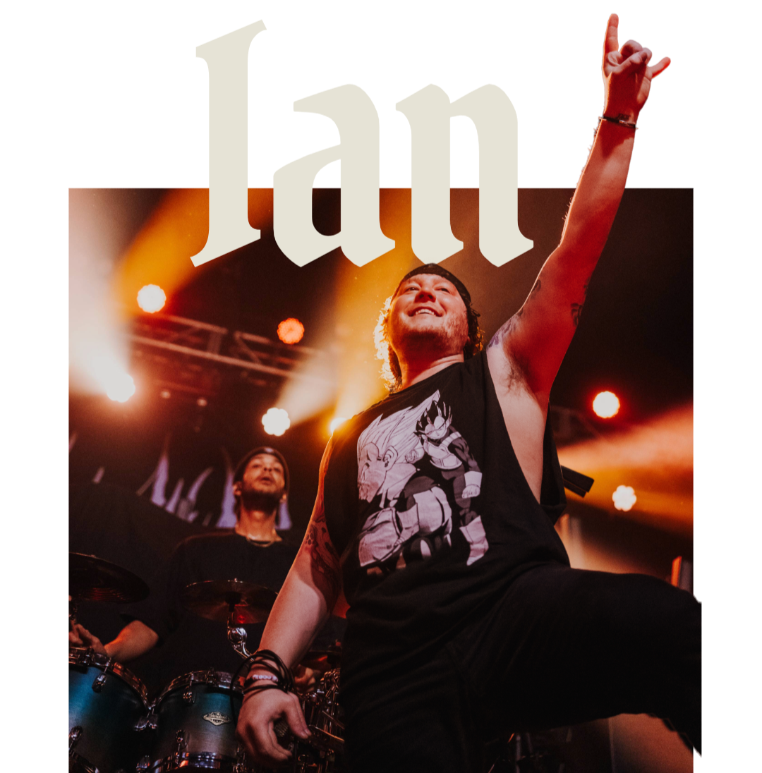 Concert scene with musicians performing on stage under colorful lights, one person in the foreground raises a hand and smiles, with a band member playing drums in the background.