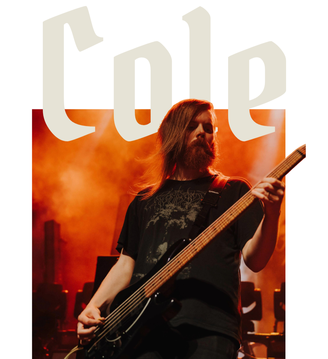 A musician with long hair and a beard playing a bass guitar on stage with orange lighting and fog, with a large stylized logo in the background.